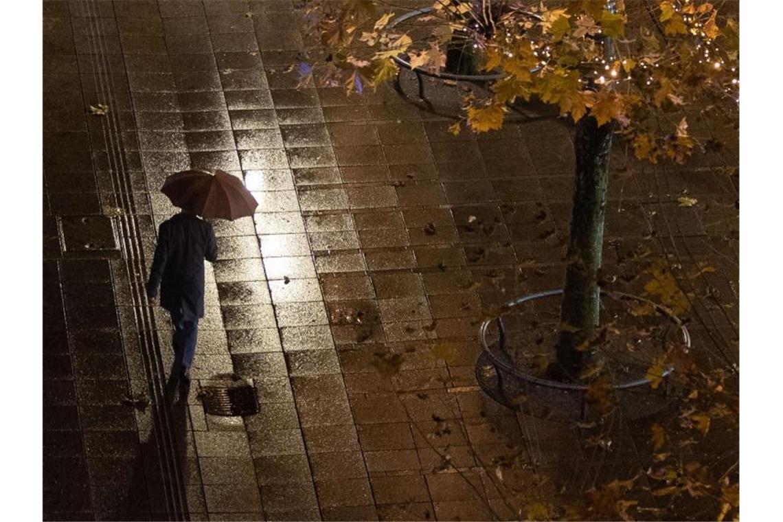 Regen, Wind und teils Schnee im Südwesten Ein Mann geht im Regen an Bäumen vorbei. Foto: Marijan Murat/dpa
