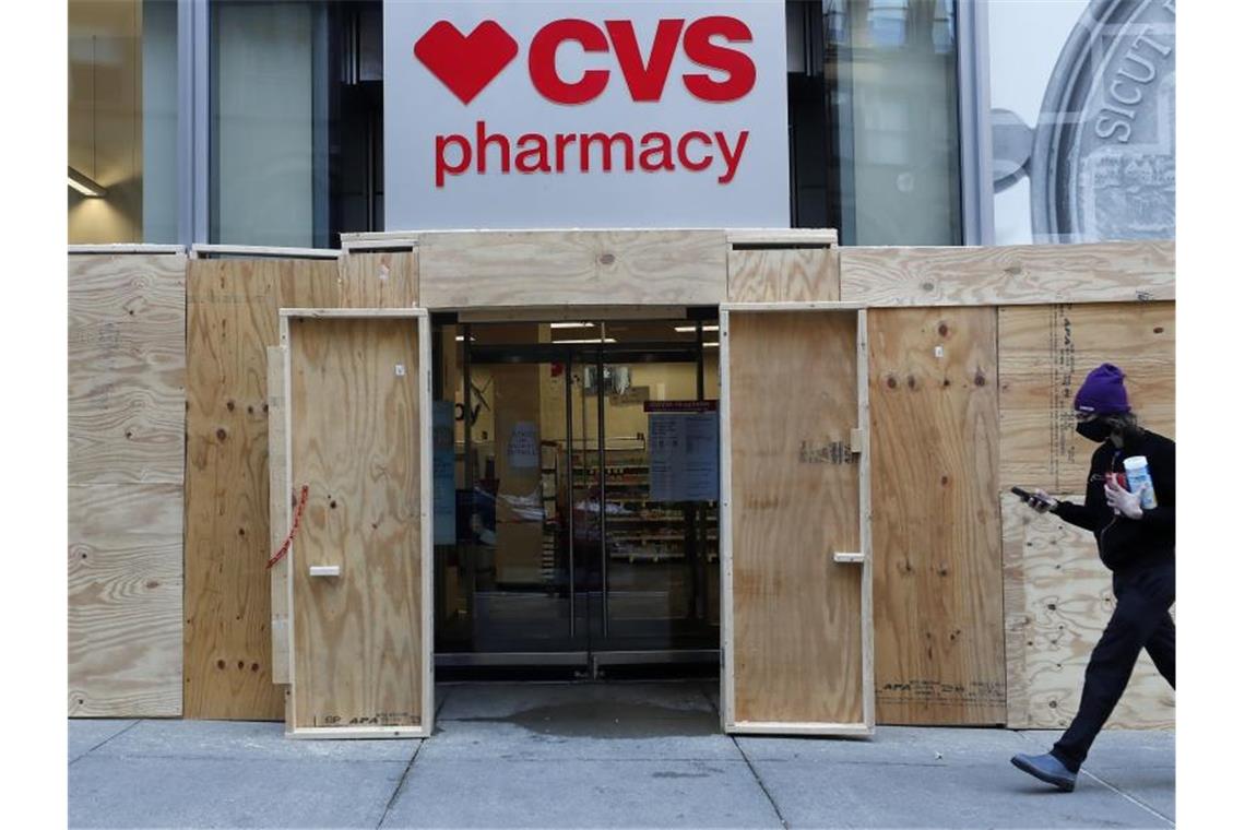 Ein Mann geht in Boston an einem mit Brettern vernagelten Geschäft der CVS-Apotheke vorbei. (Archivbild). Foto: Michael Dwyer/AP/dpa