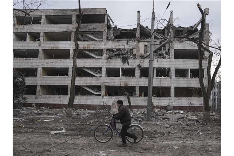 Ein Mann geht mit einem Fahrrad durch eine von Schutt übersäte Straße. Foto: Evgeniy Maloletka/AP/dpa