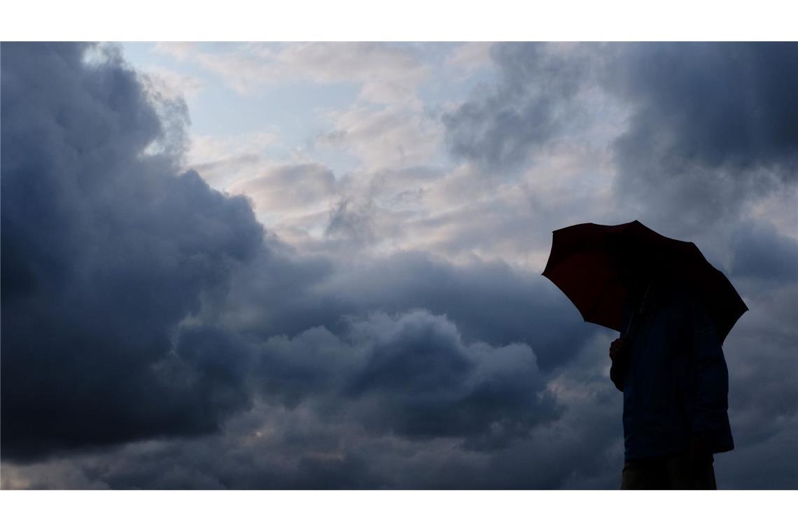 Ein Mann geht mit einem Regenschirm vor aufziehenden dunklen Wolken spazieren. (Symbolbild)