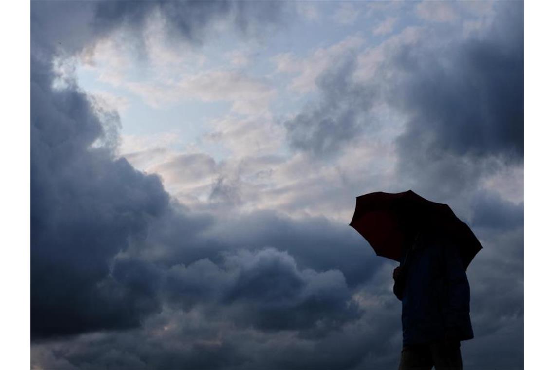 Ein Mann geht mit einem Regenschirm vor aufziehenden dunklen Wolken spazieren. Foto: Martin Gerten/Archivbild
