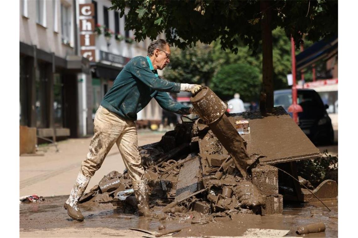 Nach der Flut: Milliarden Euro für den Wiederaufbau Ein Mann gießt nach der Hochwasserkatastrophe im nordrhein-westfälischen Gemünd Schlammreste auf einen Haufen von Schutt aus. Foto: Oliver Berg/dpa