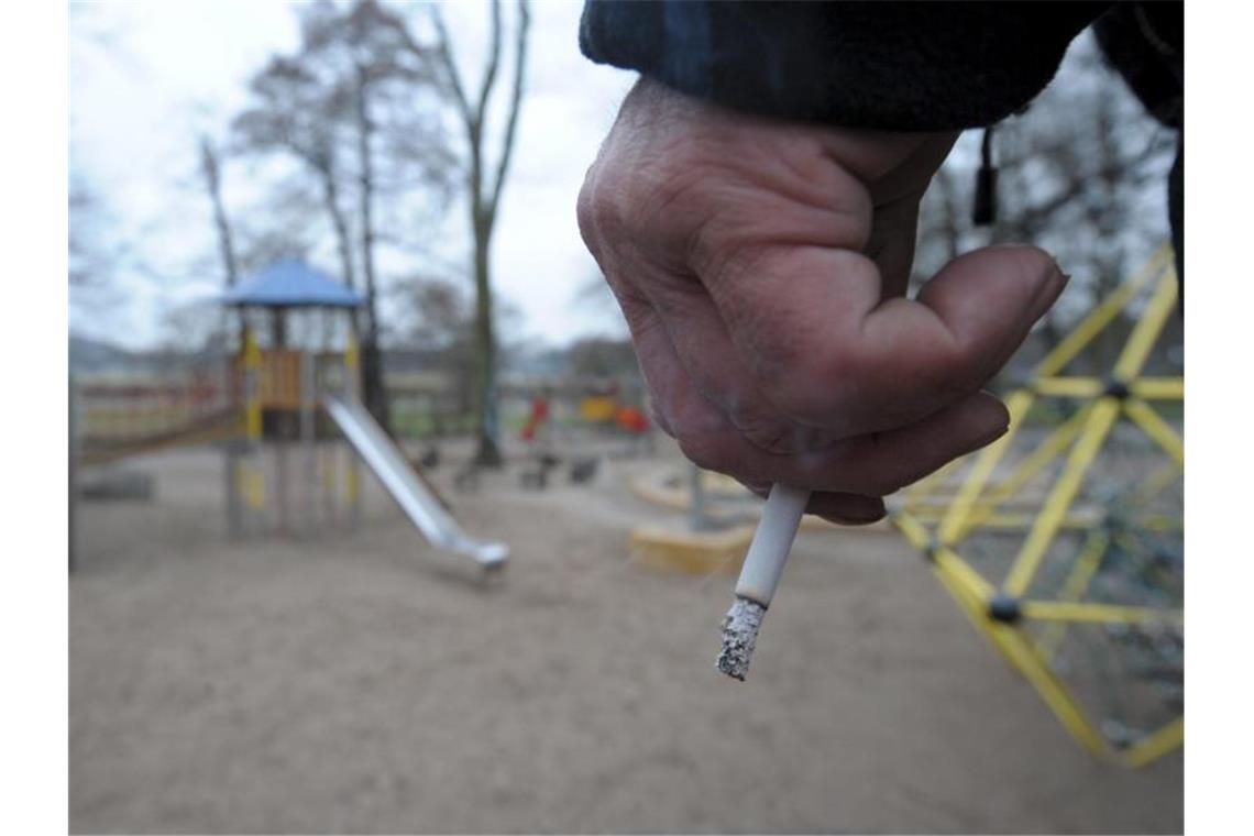 Ein Mann hält auf einem Spielplatz eine Zigarette in der Hand. Foto: Peter Endig/zb/dpa