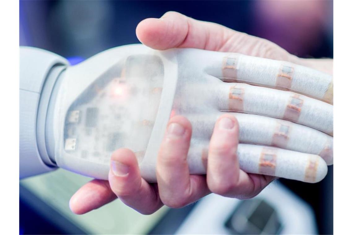 Ein Mann hält die Hand eines bionischen Roboters. Foto: Hauke-Christian Dittrich/dpa/Symbolbild