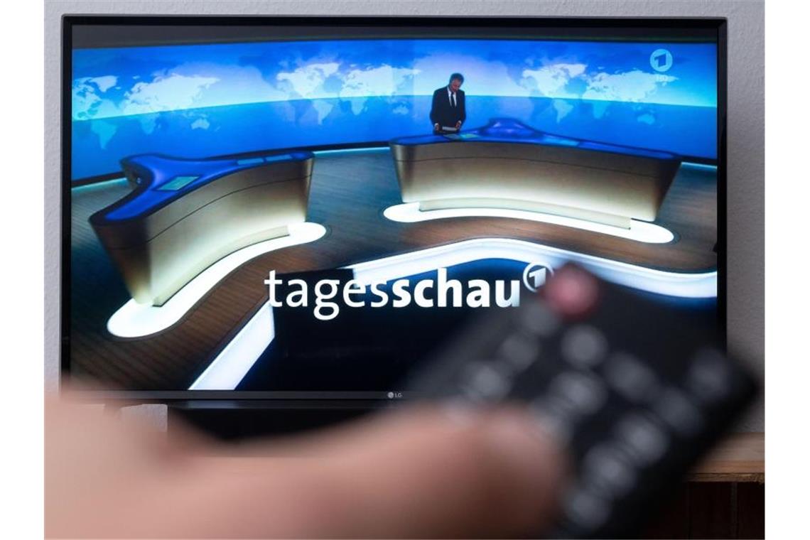 Ein Mann hält eine Fernbedienung vor einen Fernseher, auf dem die Tagesschau läuft. (Symbolbild). Foto: Marius Becker/dpa