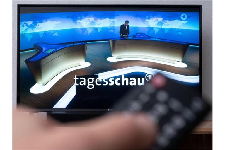 Ein Mann hält eine Fernbedienung vor einen Fernseher, auf dem die Tagesschau läuft. (Symbolbild). Foto: Marius Becker/dpa