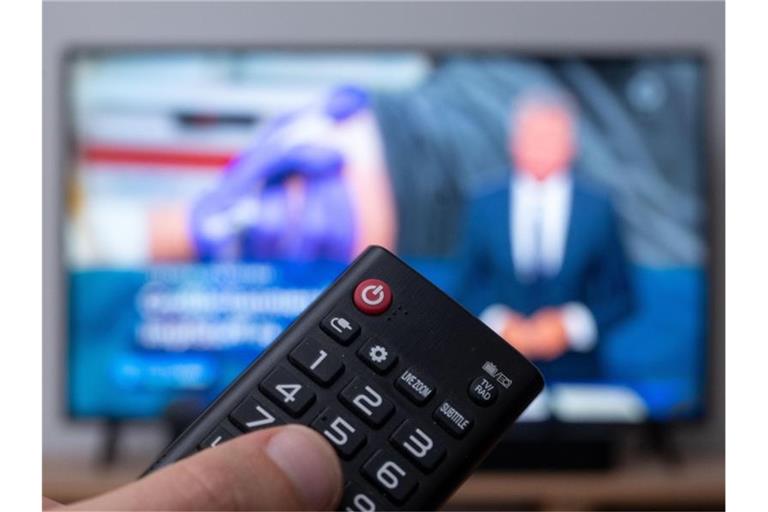 Ein Mann hält eine Fernbedienung vor einen Fernseher, auf dem die Tagesschau läuft. (Symbolbild). Foto: Marius Becker/dpa