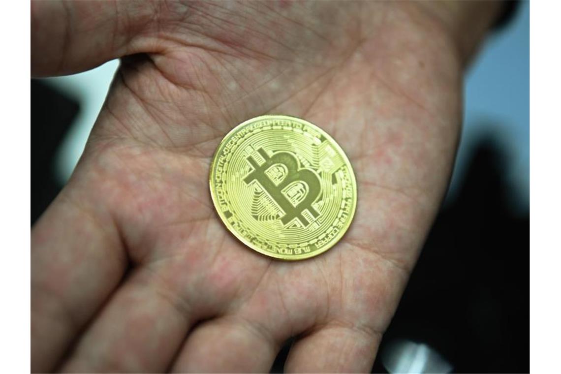 Ein Mann hält eine nachgemachte Münze mit dem Bitcoin-Logo in den Händen. Foto: Nicolas Armer/dpa
