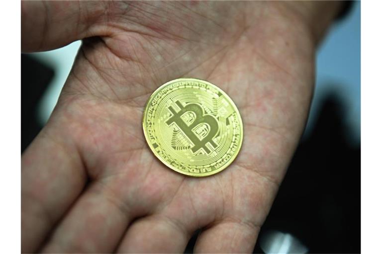 Ein Mann hält eine nachgemachte Münze mit dem Bitcoin-Logo in den Händen. Foto: Nicolas Armer/dpa