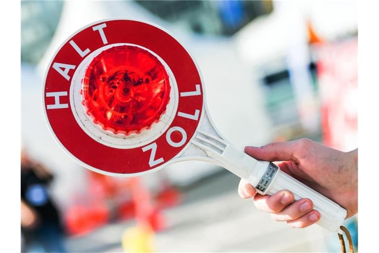 Ein Mann hält eine Winkerkelle mit der Aufschrift „Halt Zoll“ in der Hand. Foto: picture alliance / Christophe Gateau/dpa/Symbolbild