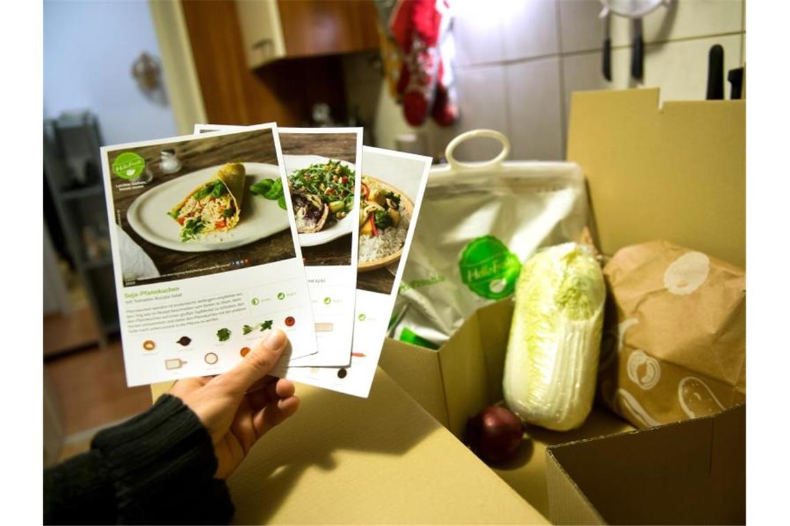 Ein Mann hält mitgelieferte Kochrezepte aus einer HelloFresh Kochbox in der Hand. Foto: picture alliance / dpa