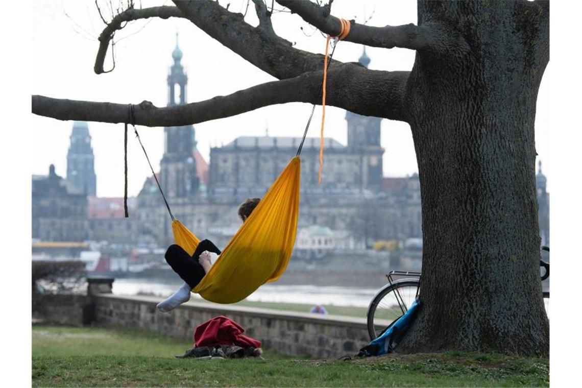 Ein Mann hat es sich am Ufer der Elbe vor der Kulisse der Dresdner Altstadt in einer Hängematte gemütlich gemacht. Foto: Sebastian Kahnert/dpa-Zentralbild/dpa