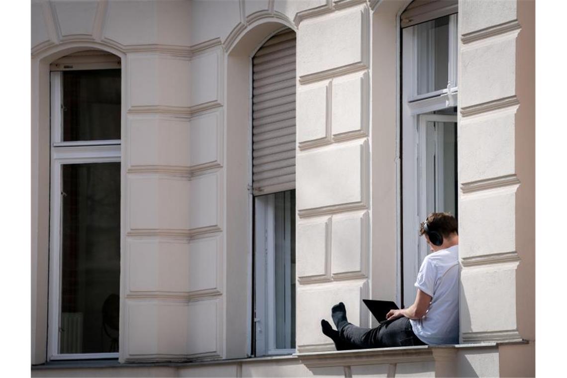 Ein Mann hat sein Homeoffice auf die sonnige Fensterbank seiner Wohnung in Berlin verlegt. Foto: Kay Nietfeld/dpa