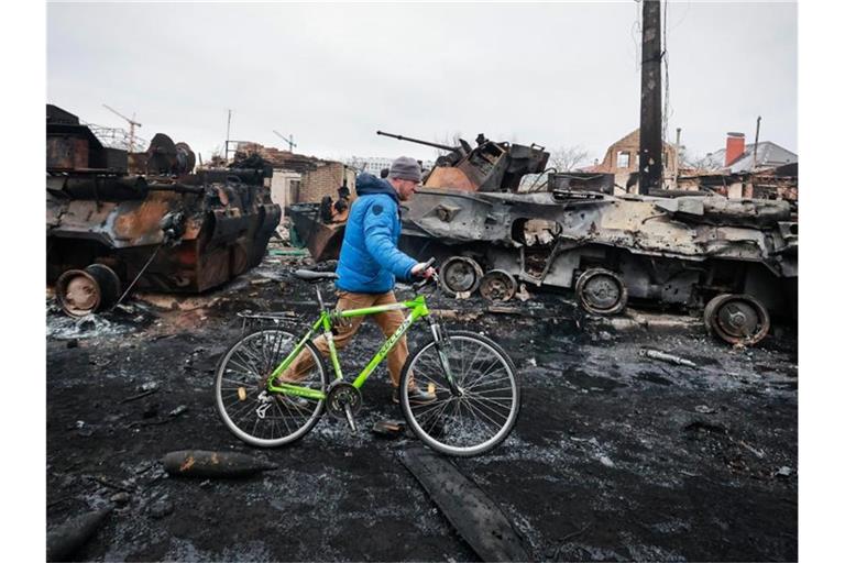 Ein Mann in Butscha schiebt sein Fahrrad an den Überresten eines russischen Militärfahrzeugs vorbei. Foto: Serhii Nuzhnenko/AP/dpa