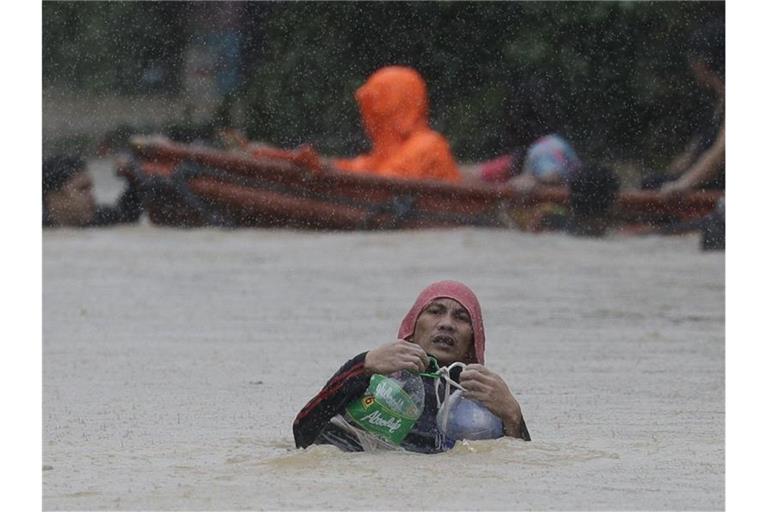 Ein Mann in Marikina benutzt Plastikbehälter, um sich beim Überqueren einer überfluteten Straße über Wasser zu halten. Foto: Aaron Favila/AP/dpa