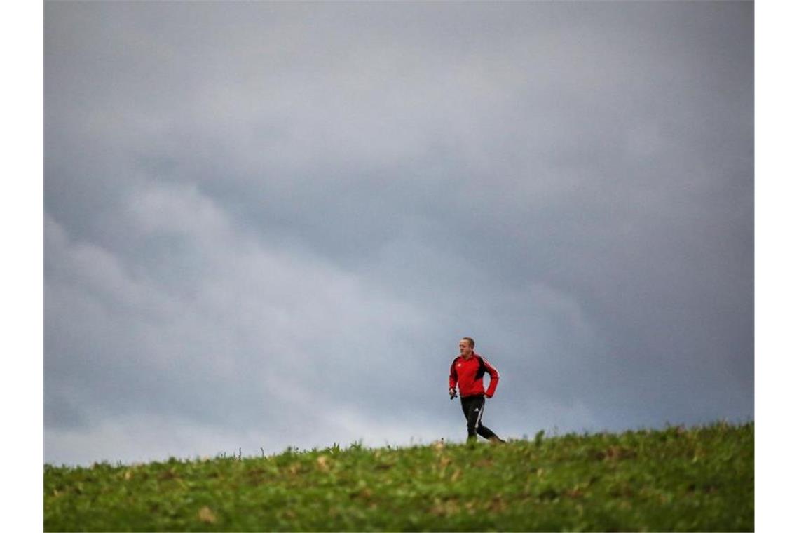 Ein Mann joggt bei bewölktem Wetter über einen Feldweg. Foto: Thomas Warnack/dpa/Archivbild