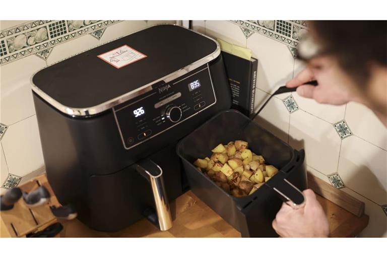 Ein Mann kocht in seiner Küchen mit einer Heißluftfritteuse (Airfryer) ein Gericht aus Kartoffelstücken und gebratenem Hühnerfleisch. (Symbolbild)