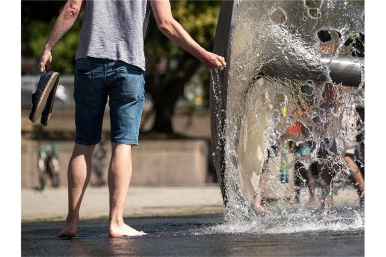 Ein Mann kühlt sich an einem Brunnen ab. Foto: Marius Becker/dpa