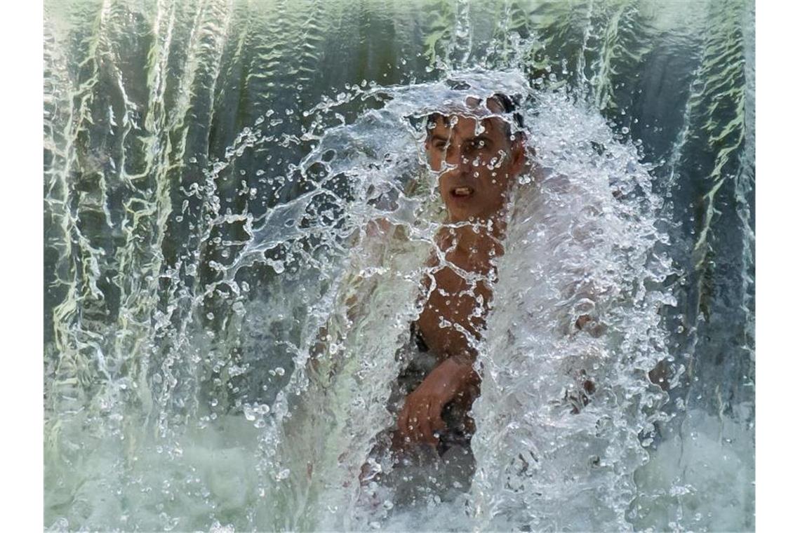 Extreme Junihitze - Wetterrekorde verlagern sich nach vorn Ein Mann kühlt sich an einem kleinen Wasserfall im Eisbach im Englischen Garten ab. Foto: Peter Kneffel