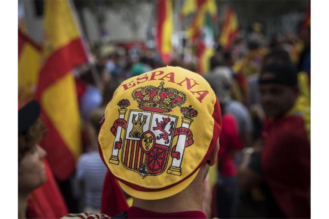Ein Mann mit einer Mütze auf der das spanische Wappen zu sehen ist, nimmt an einer Demonstration, die während des Nationalfeiertags in Spanien stattfindet, teil. Foto: Santi Palacios/AP/dpa