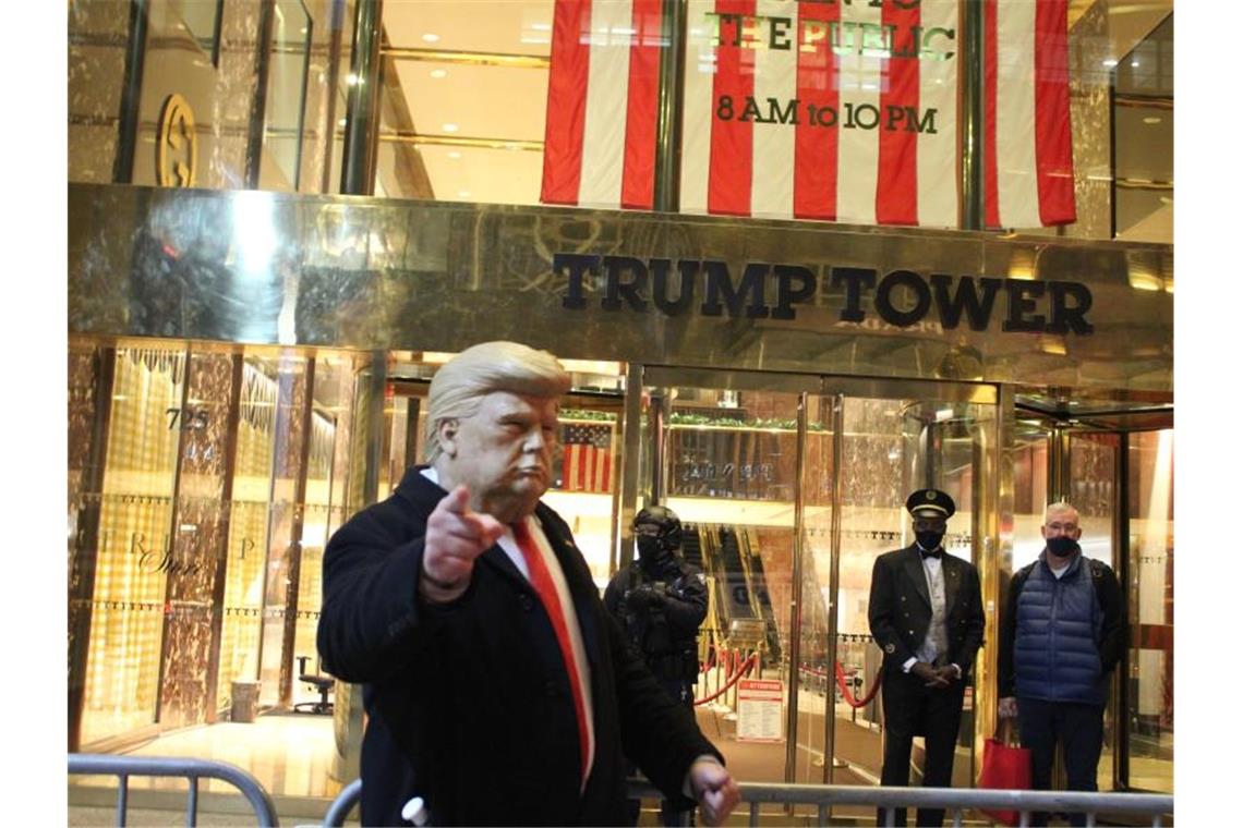 Ein Mann mit einer Trump-Maske in der Hand gestikuliert vor dem Trump Tower, der von einem Polizisten einer Spezialeinheit des NYPD auf der 5th Avenue in Manhattan am Vorabend der Präsidentschaftswahlen gesichert wird. Foto: Marie Le Ble/ZUMA Wire/dpa