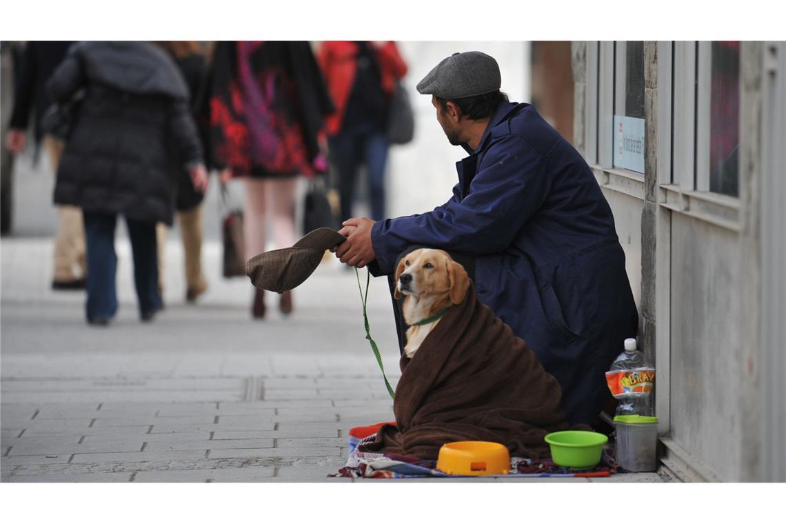 Ein Mann mit Hund bettelt in einer Fußgängerzone um Geld.