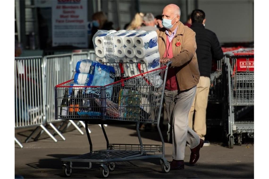 Ein Mann mit Maske schiebt einen Einkaufswagen voll mit Dosen, Getränken und Toilettenpapier in Birmingham an einem Costco-Markt vorbei. Foto: Jacob King/PA Wire/dpa
