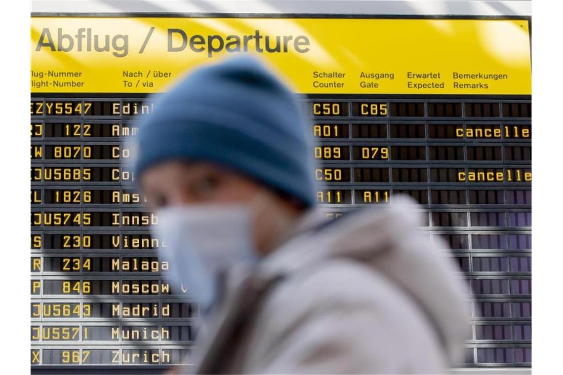 Ein Mann mit Mundschutz steht am Flughafen Berlin-Tegel vor der Anzeigetafel der Abflüge. Foto: Christoph Soeder/dpa