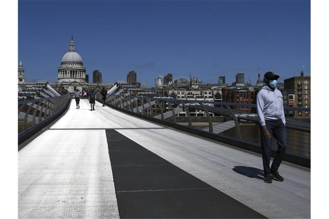 Ein Mann mit Mundschutz überquert während der anhaltenden Ausgangsbeschränkungen die fast menschenleere Millennium Bridge in London. Foto: Alberto Pezzali/AP/dpa