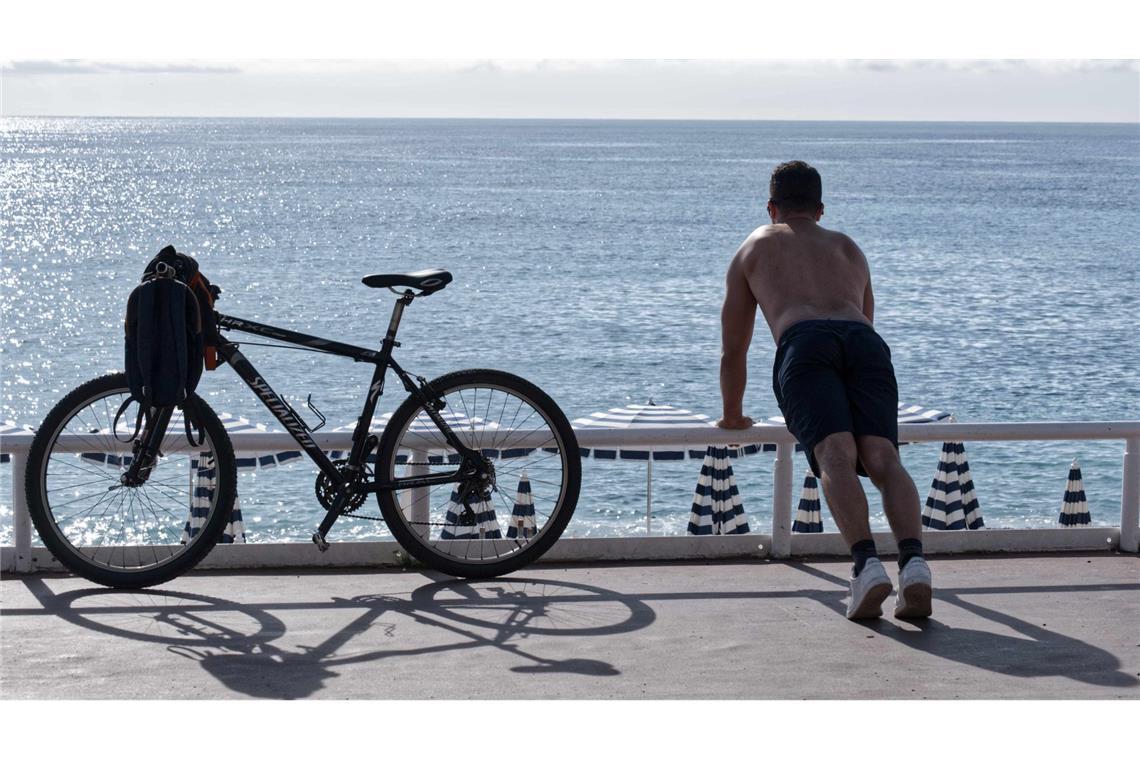 Ein Mann mit nacktem Oberkörper macht am Strand von Nizza neben seinem Fahrrad Übungen. (Archivbild)