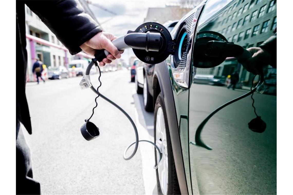 Ein Mann nimmt an einem Auto mit Plug-in-Hybrid-Antrieb in Berlin-Mitte den Ladestecker raus. Foto: Christoph Soeder/dpa