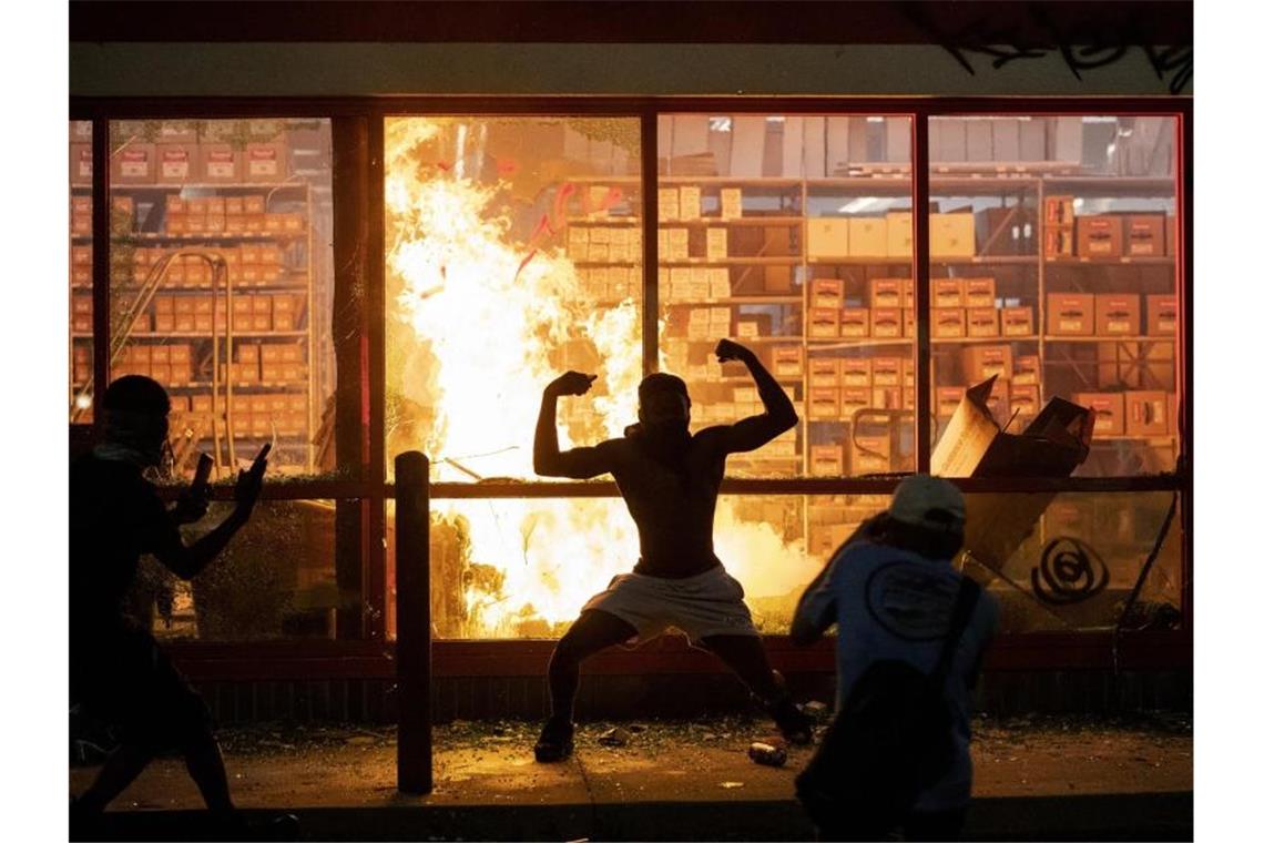 Ein Mann posiert während der gewaltsamen Proteste in Minneapolis vor einem Feuer einem Geschäft. Foto: Carlos Gonzalez/Star Tribune/AP/dpa