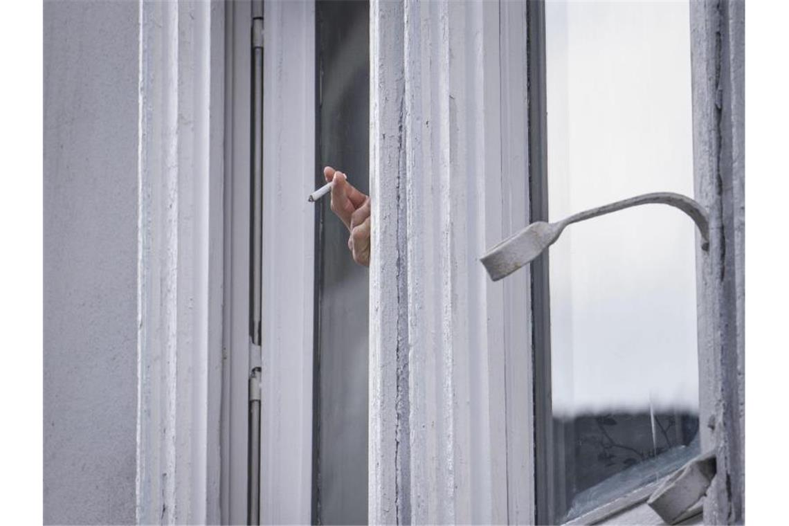 Ein Mann raucht während der Ausgangsbeschränkung am Fenster. Foto: Frank Rumpenhorst/dpa