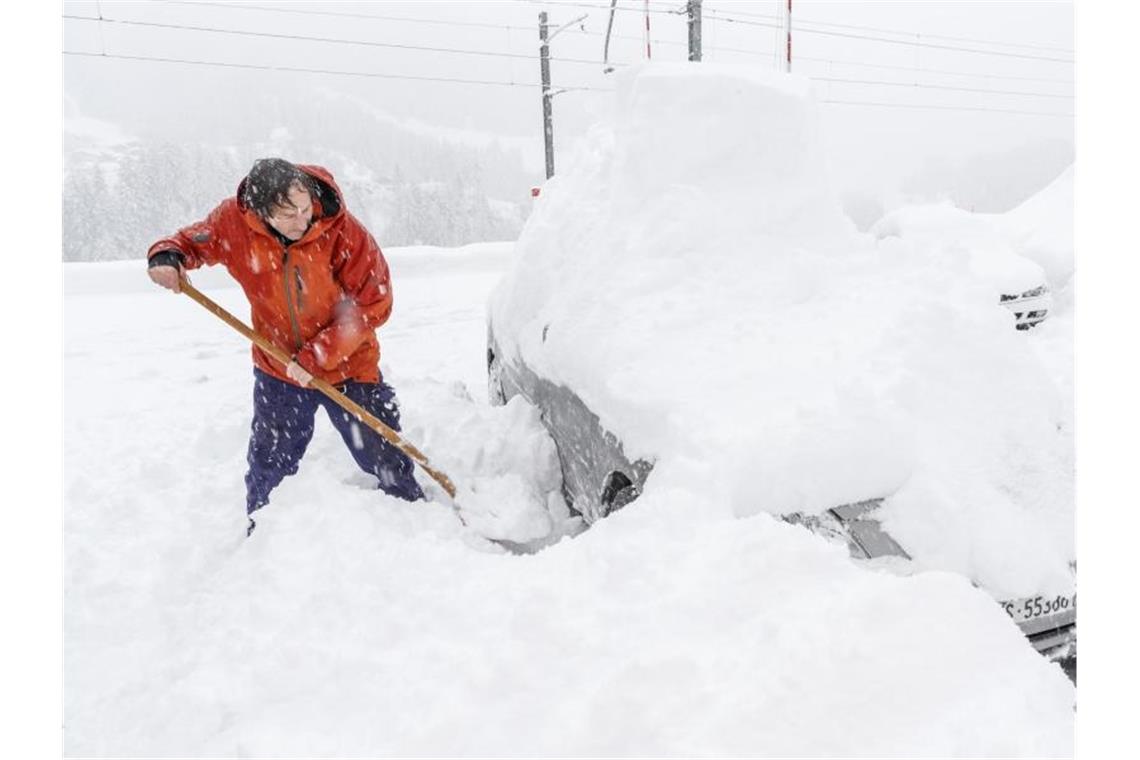 Ein Mann schaufelt sein eingeschneites Auto frei. Viele Walliser Täler sind wegen dem starken Schneefall von der Außenwelt abgeschnitten. Foto: Andrea Soltermann/KEYSTONE/dpa