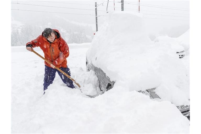Ein Mann schaufelt sein eingeschneites Auto frei. Viele Walliser Täler sind wegen dem starken Schneefall von der Außenwelt abgeschnitten. Foto: Andrea Soltermann/KEYSTONE/dpa