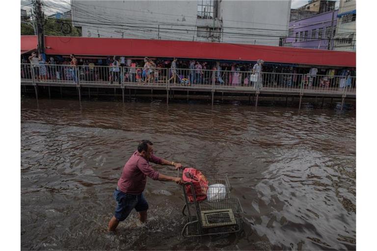 Ein Mann schiebt einen Einkaufswagen durch eine überschwemmte Straße in Manaus. Foto: Lucas Silva/dpa