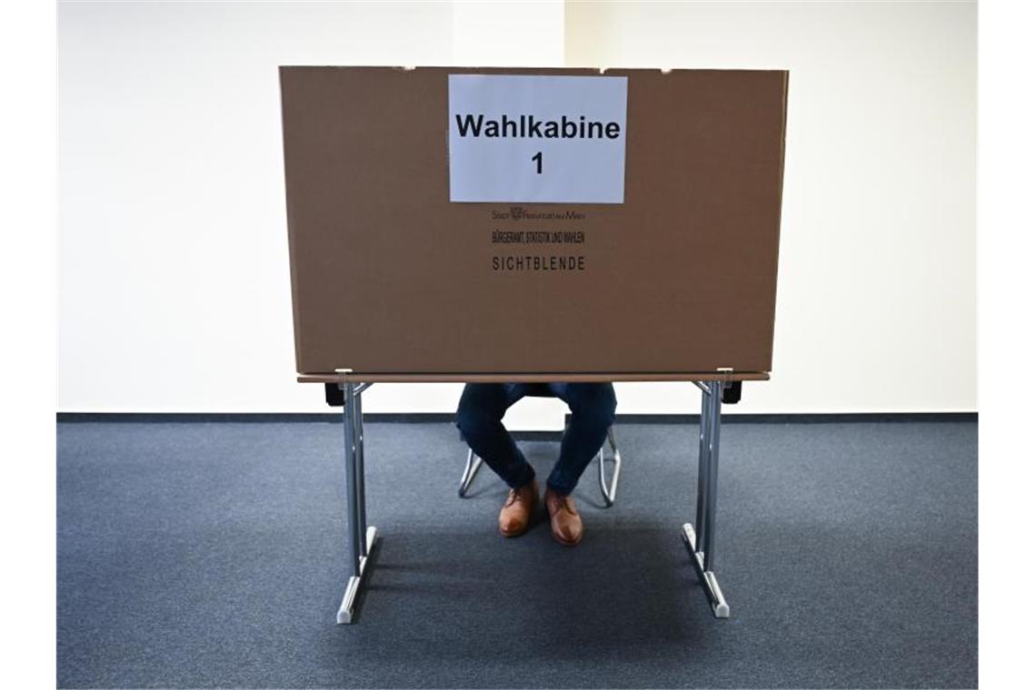 Ein Mann sitzt im Wahlraum eines Briefwahllokals hinter einer Wahlkabine. Foto: Arne Dedert/dpa/Archivbild