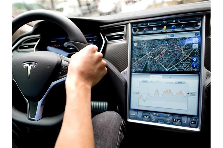 Ein Mann sitzt in einem Tesla Model S am Lenkrad, neben ihm ein großer Monitor im Armaturenbrett. Foto: picture alliance / dpa