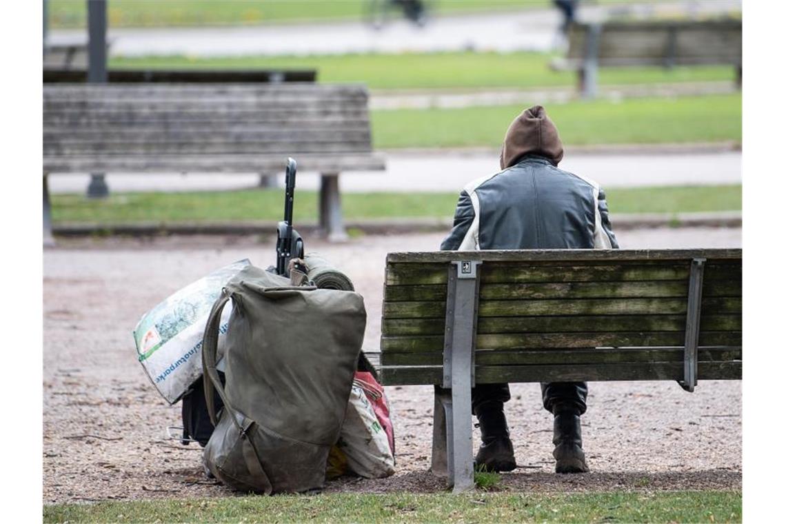Ein Mann sitzt mit seinen Habseligkeiten auf einer Parkbank. Foto: Sebastian Gollnow/dpa