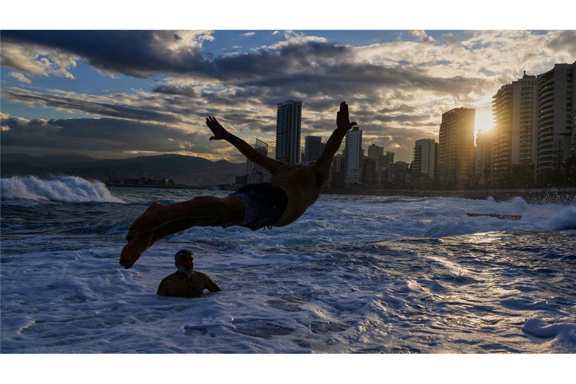 Ein Mann springt bei Temperaturen um die 10 Grad Celsius ins Mittelmeer, während die Sonne über Beirut aufgeht.