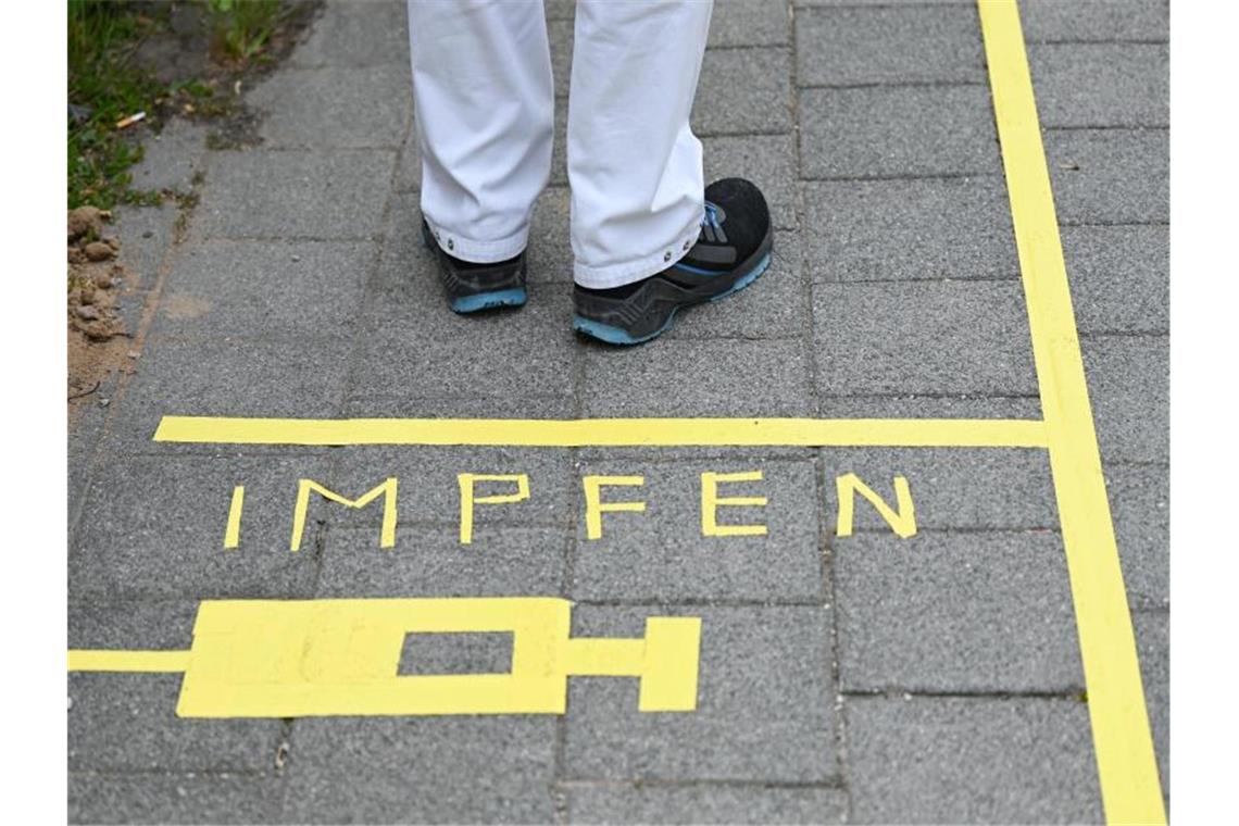 Ein Mann steht am Covid-19 Impfcenter hinter einer Bodenmarkierung mit der Aufschrift "Impfen" und einer Spritze. Foto: Arne Dedert/dpa/POOL/dpa/Symbolbild