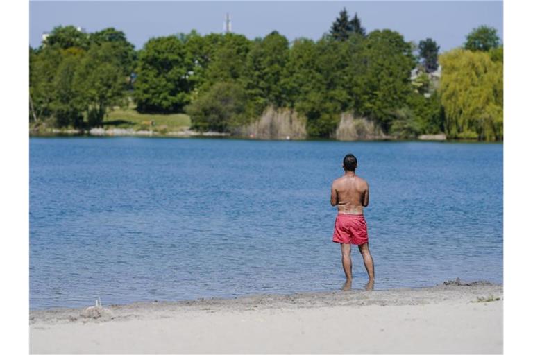 Ein Mann steht am Ufer eines Badesees mit den Füßen im Wasser. Foto: Uwe Anspach/dpa/Archivbild