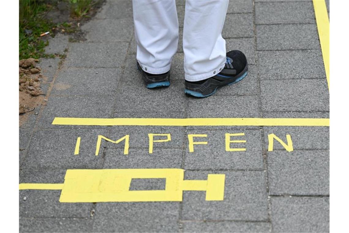 Ein Mann steht an einem Covid-19-Impfcenter hinter der Bodenaufschrift "Impfen". Foto: Arne Dedert/dpa/POOL/dpa/Symbolbild