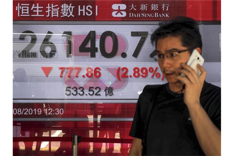 Ein Mann telefoniert in Hongkong vor einer Anzeigetafel mit dem Hong Kong Composite Index. Foto: Kin Cheung/AP