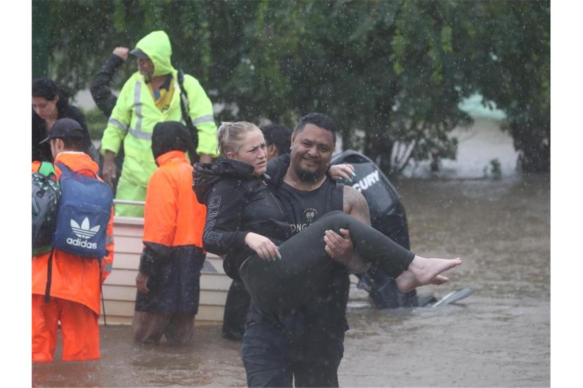 Historische Überschwemmungen in Australien Ein Mann trägt eine Frau durch das Hochwasser einer überschwemmten Straße im australischen Lismore. Foto: Jason O‚äôbrien/AAP/dpa
