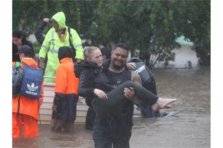 Ein Mann trägt eine Frau durch das Hochwasser einer überschwemmten Straße im australischen Lismore. Foto: Jason O‚äôbrien/AAP/dpa