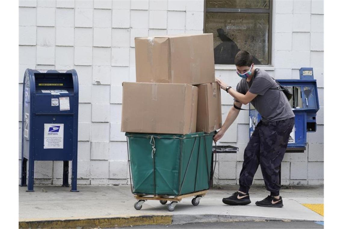 Ein Mann trägt eine Schutzmaske während er große Paketboxen von einem Postamt in Los Angeles in ein Fahrzeug transportiert. Foto: Damian Dovarganes/AP/dpa