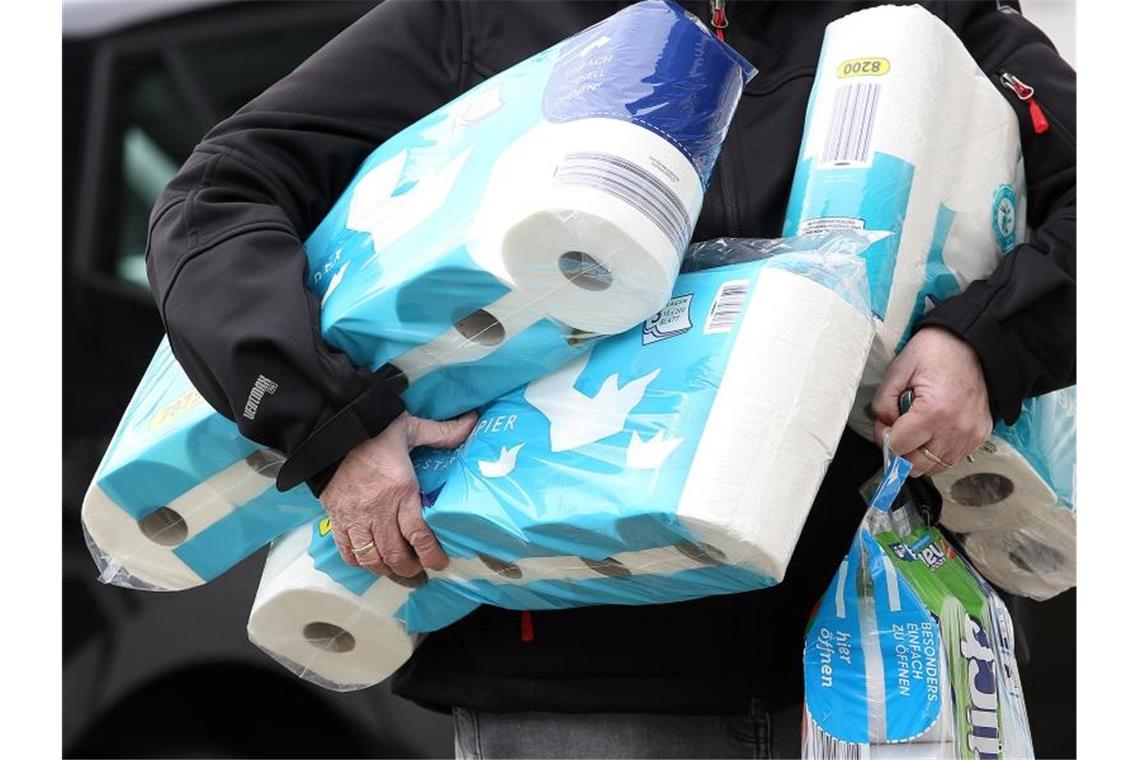 Ein Mann trägt eingekauftes Toilettenpapier und Küchenrollen aus einem Supermarkt. Foto: Rene Traut/dpa