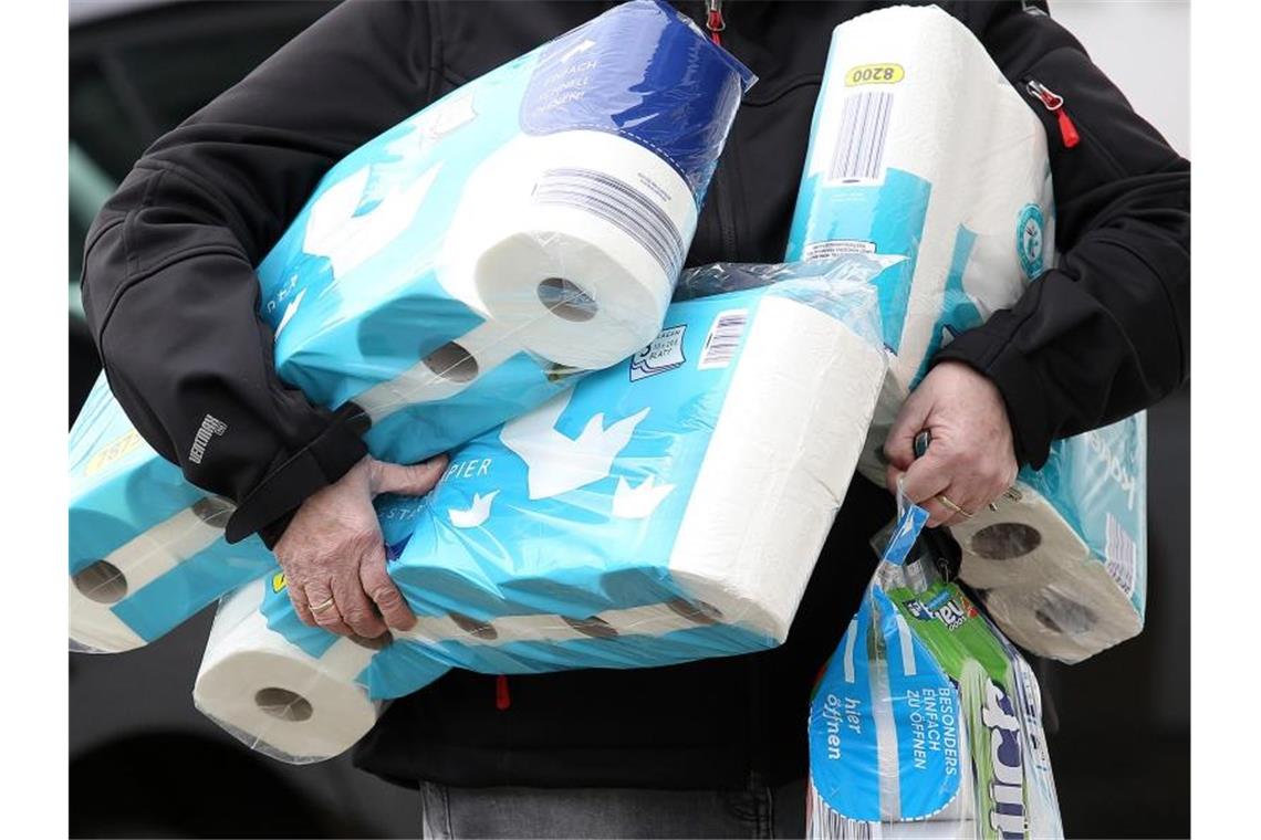 Ein Mann trägt eingekauftes Toilettenpapier und Küchenrollen aus einem Supermarkt. Foto: Rene Traut/dpa/Archivbild