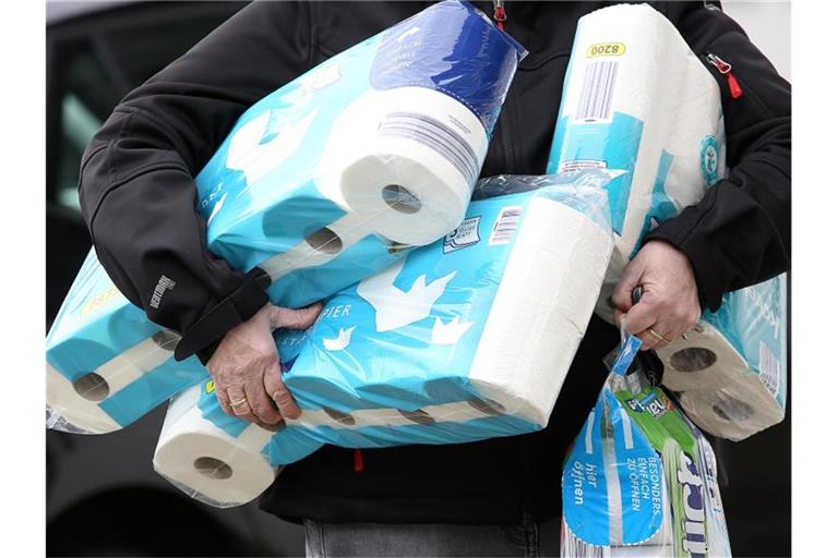 Ein Mann trägt eingekauftes Toilettenpapier und Küchenrollen aus einem Supermarkt. Foto: Rene Traut/dpa